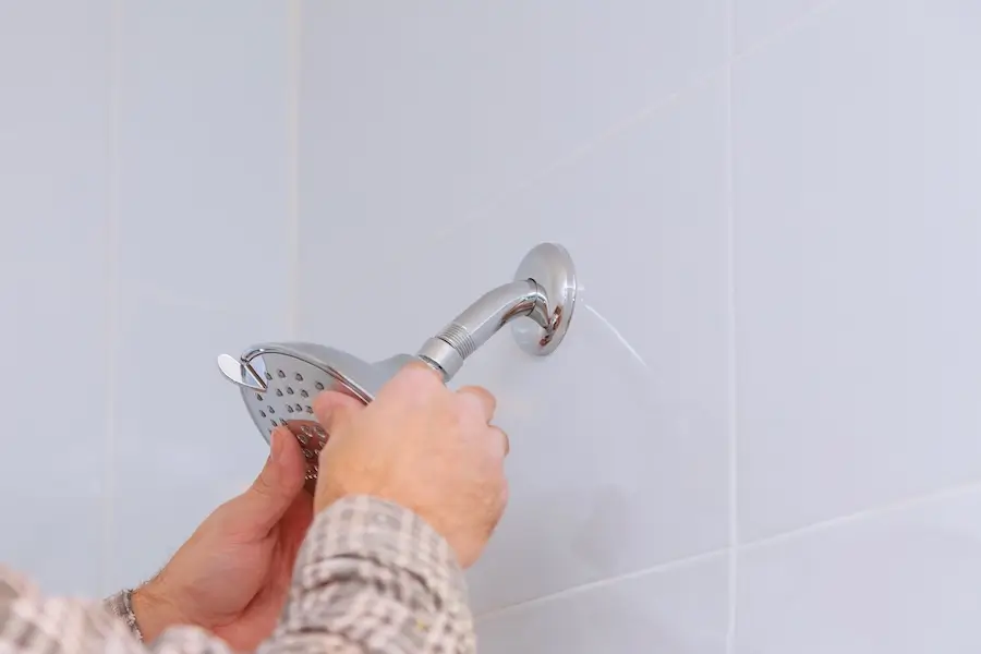 Homeowner replacing shower head in their bathroom.