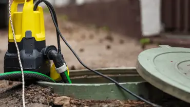 Close-up of a portable sump pump next to an open access hatch in a yard.