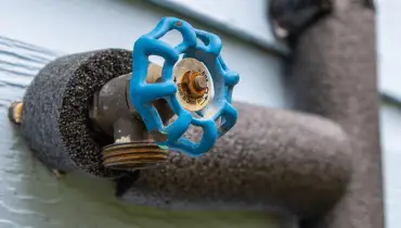 Close-up of an outdoor hose bib with blue valve handle, wrapped in foam pipe insulation.