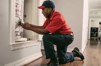 A Mr. Rooter plumber using a wrench to repair a water heater