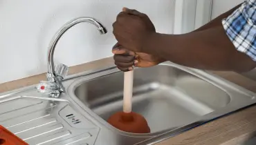 A man using a plunger in a clogged kitchen sink.