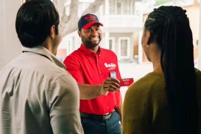 A courteous Mr. Rooter plumber smiling and showing his business card to his customers at their front door.