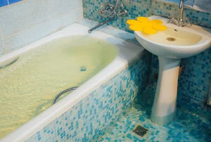 Flooded, blue-tiled bathroom in need of an emergency plumber in Charlotte