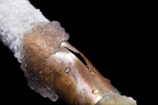A copper pipe covered in frost and ice with a crack in the center.