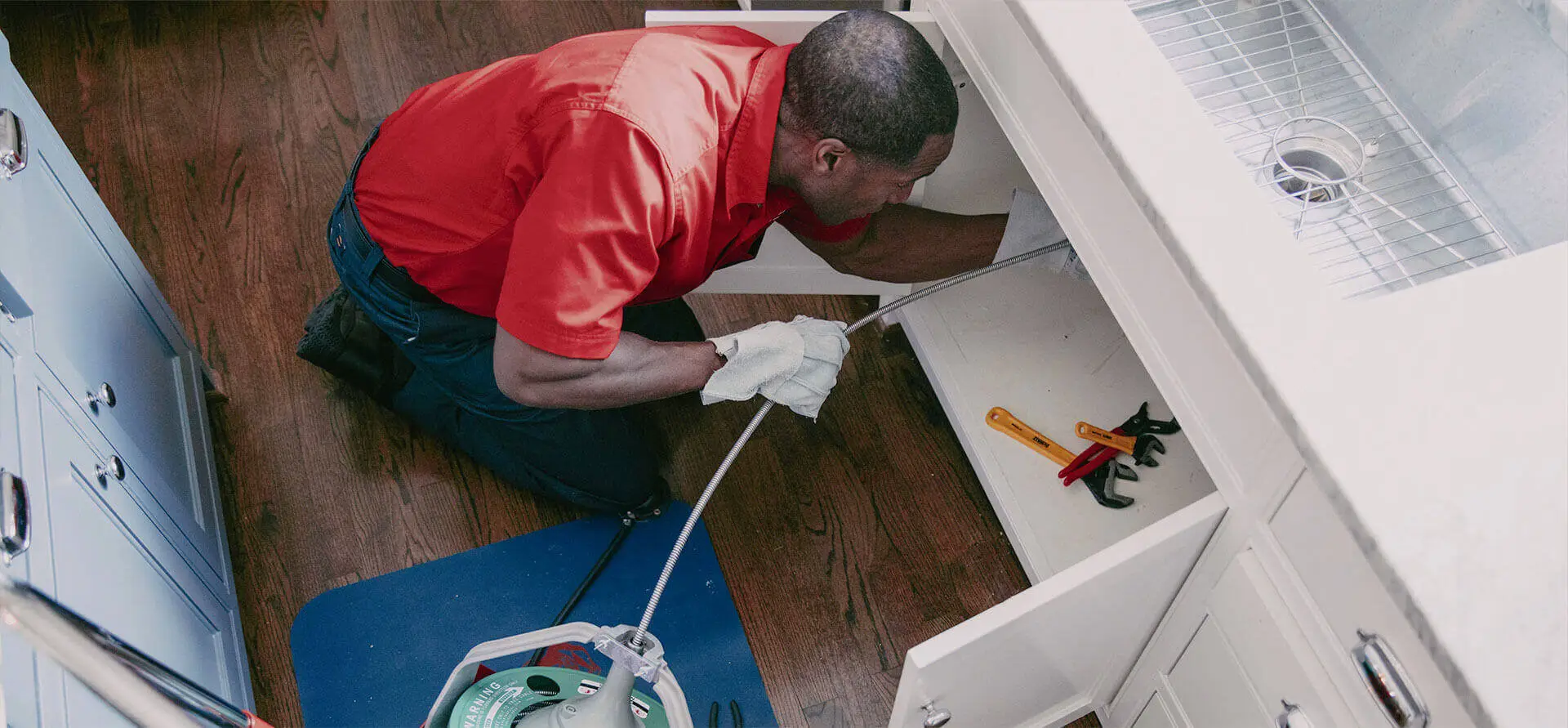 Mr. Rooter plumber using a snake to clear a kitchen sink drain