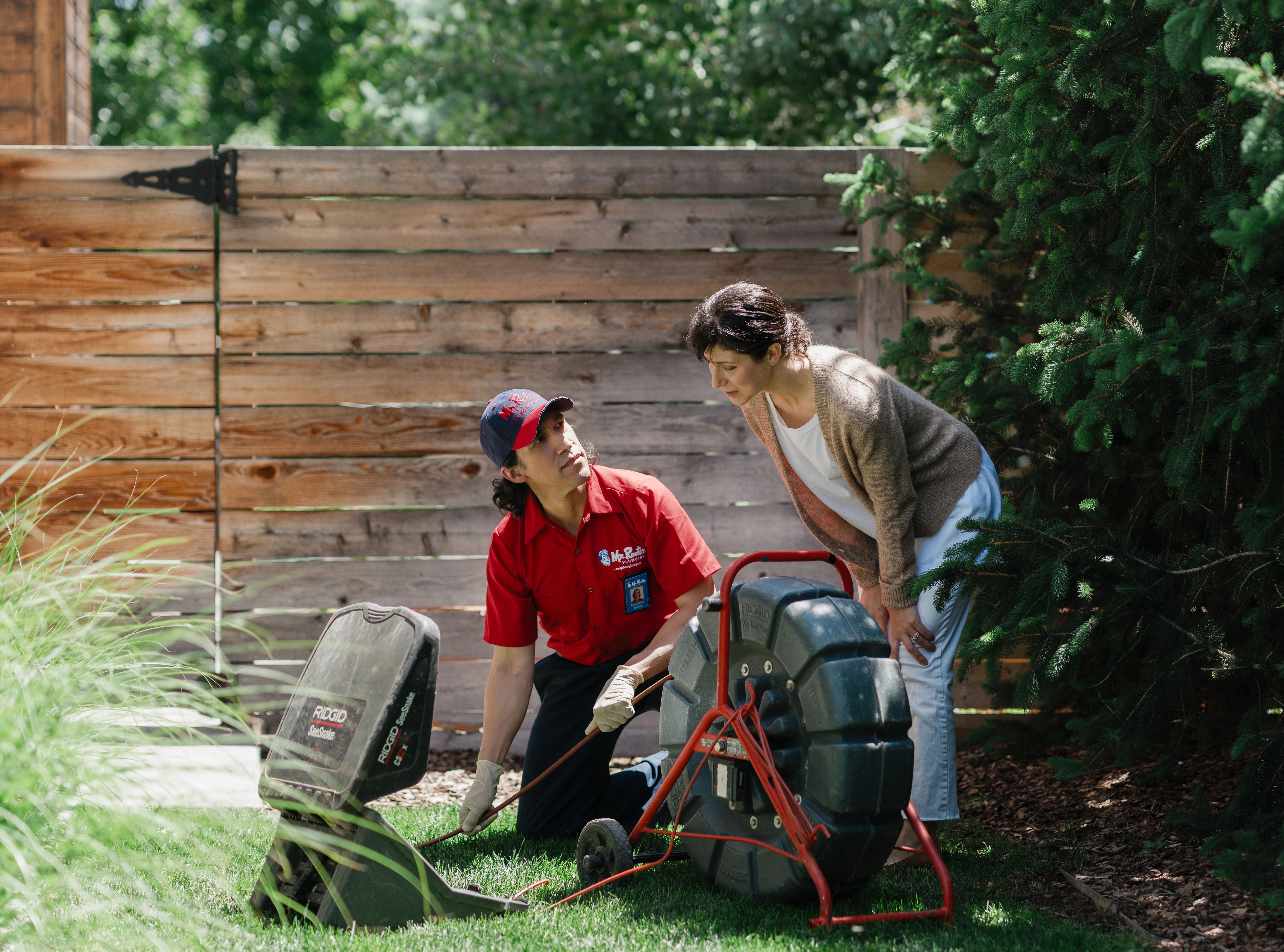 Mr. Rooter Plumbing service professional showing a homeowner sewer line inspection equipment during an outdoor evaluation.
