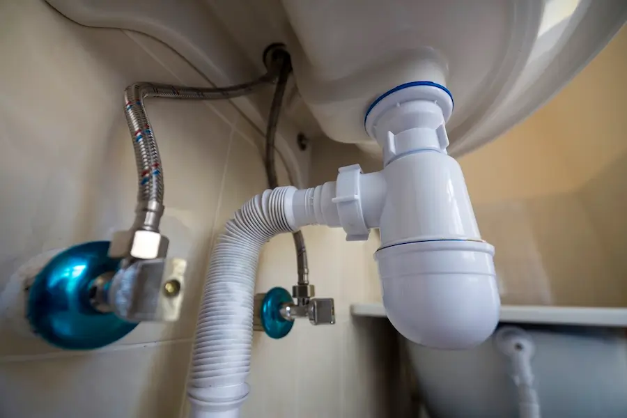 Underside of a sink showing the trap primer connected to the plumbing system beneath the basin.
